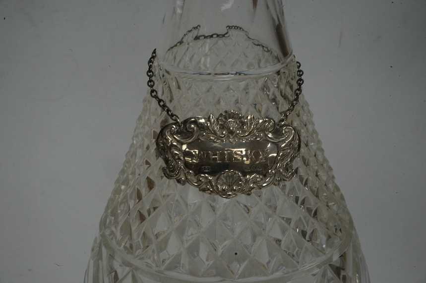 An early 1970's silver collared cut glass decanter and stopper, London, 1972, height 37cm, together with a 1960's silver whiskey label. Condition - fair to good.